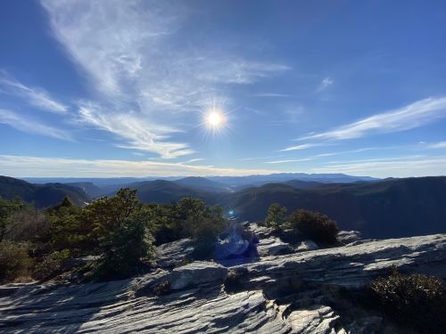 A scenic mountain view with a bright sun shining over distant peaks and a clear blue sky.