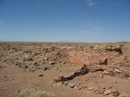 Ruins of an ancient stone structure in a barren landscape with distant mountains under a clear blue sky.