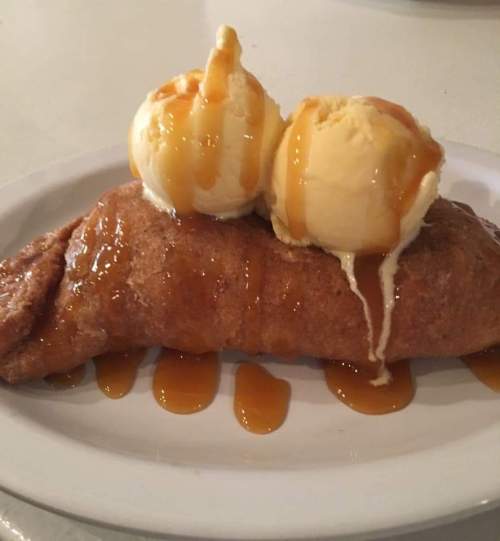 A golden-brown pastry topped with two scoops of vanilla ice cream and drizzled with caramel sauce.