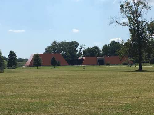 A modern building with angular red roofs set in a grassy landscape under a clear blue sky.