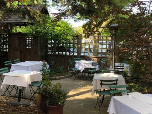 A serene outdoor dining area with white tablecloths, green chairs, and lush greenery, surrounded by wooden fences.