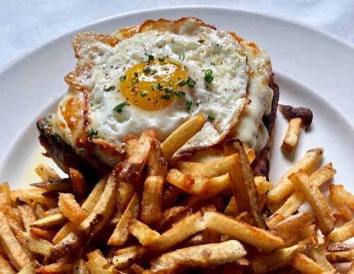 A plate of crispy French fries topped with a burger featuring a fried egg and melted cheese.