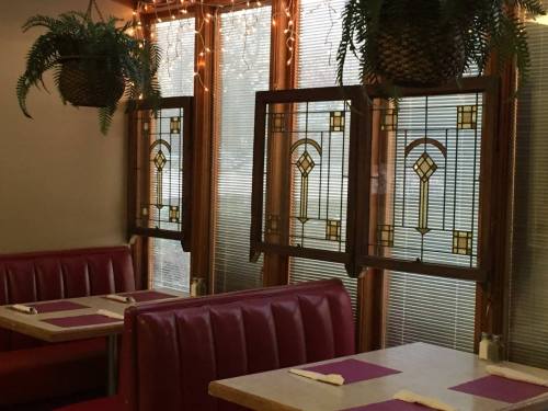 Cozy restaurant interior featuring stained glass windows, red booths, and potted ferns. Warm, inviting atmosphere.