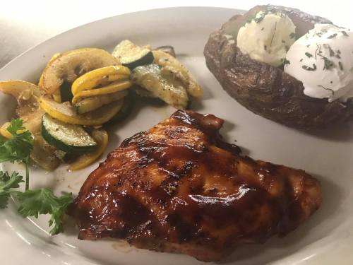 Grilled chicken with barbecue sauce, roasted vegetables, and a baked potato topped with sour cream and herbs.