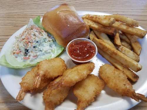 A plate with fried shrimp, coleslaw on lettuce, a roll, fries, and a small cup of dipping sauce.