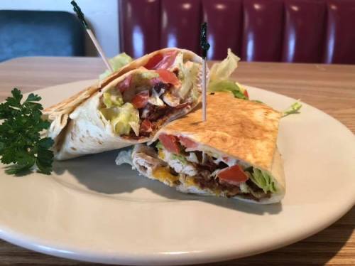A sliced wrap filled with chicken, lettuce, tomatoes, and cheese, garnished with parsley on a plate.