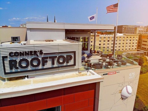 Aerial view of a rooftop bar with a sign reading "Connor's Rooftop," featuring a baseball and American flag in the background.
