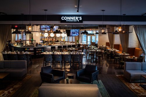 Interior of Conner's Kitchen + Bar, featuring a bar area, dining tables, and modern decor in a spacious setting.