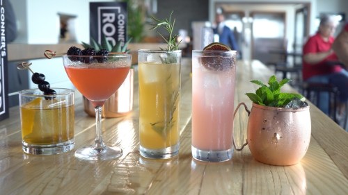 A variety of colorful cocktails on a wooden table, including a martini, a fruity drink, and a mint julep.