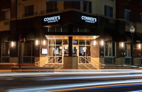 Exterior view of Conner's Kitchen & Bar at night, featuring illuminated signage and light trails from passing cars.