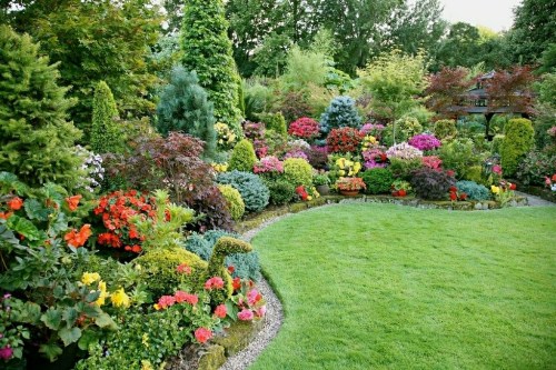 A vibrant garden filled with colorful flowers, lush greenery, and neatly arranged plants along a curved pathway.