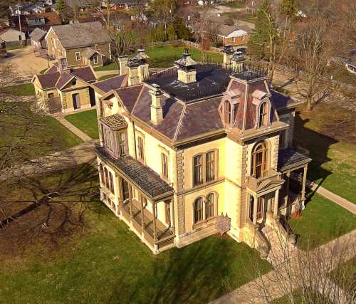 Aerial view of a large, historic mansion with a complex roof and surrounding green lawn.
