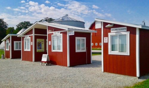 Red ticket booths with white trim, set against a blue sky, in a gravel area. One booth is labeled "OUTLINE TICKETS."