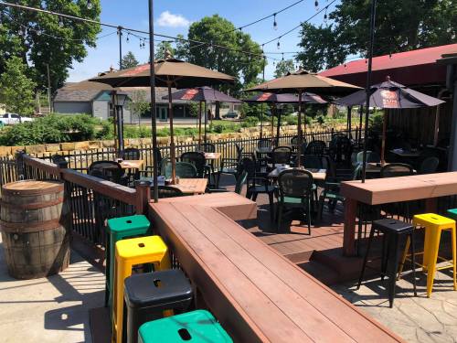 Outdoor seating area of a restaurant with umbrellas, wooden deck, and colorful stools, surrounded by greenery.