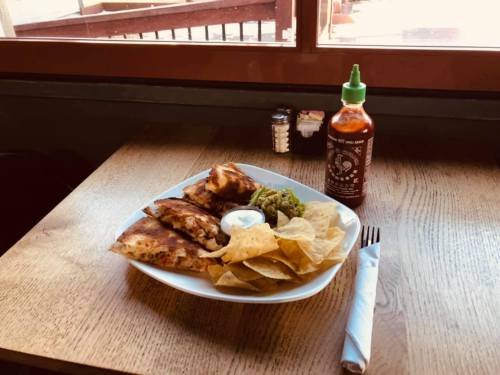 A plate of quesadillas, chips, guacamole, and a side of sour cream, with a bottle of hot sauce on a wooden table.