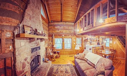 Cozy log cabin interior with a stone fireplace, wooden beams, and rustic furniture, creating a warm, inviting atmosphere.