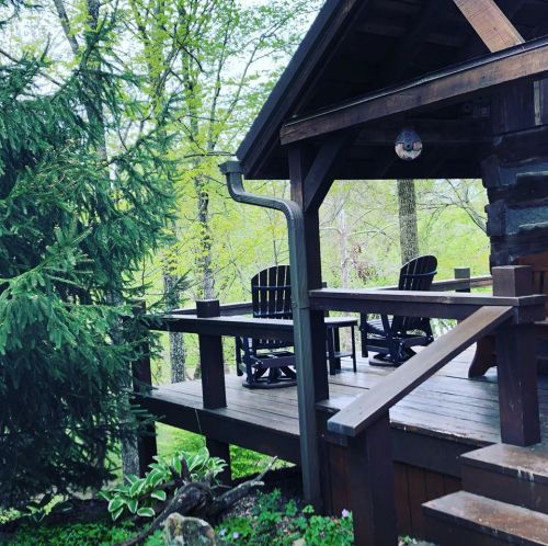A cozy wooden cabin with a porch, surrounded by lush green trees and a peaceful natural setting.