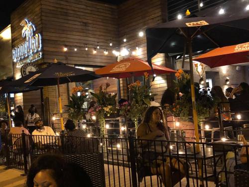 Outdoor dining scene at night, featuring patrons under umbrellas with string lights and vibrant flower arrangements.