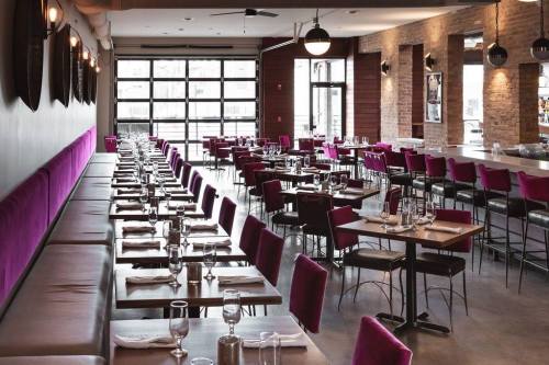 Modern restaurant interior with purple seating, wooden accents, and tables set for dining. Bright and spacious atmosphere.