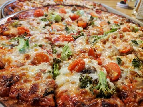 A close-up of a delicious pizza topped with cheese, tomatoes, broccoli, and other vegetables, served on a large tray.