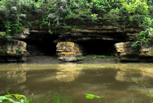 A serene river scene with rocky cliffs and lush greenery reflected in the calm water.