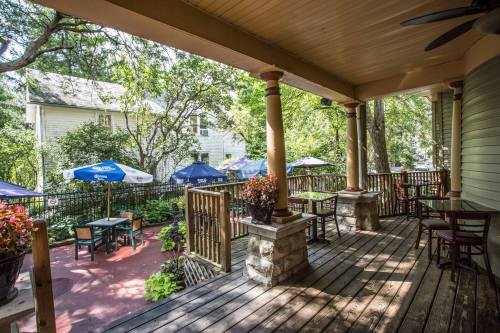 A cozy porch with wooden flooring, potted plants, and tables under umbrellas, surrounded by trees and a charming setting.