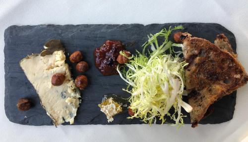 A slate platter featuring cheese, nuts, chutney, salad, and toasted bread.
