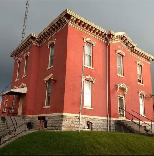 Historic red brick building with ornate details, featuring multiple windows and a staircase, set against a cloudy sky.