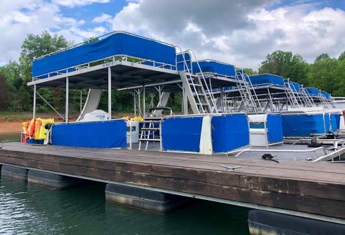 A dock with multiple blue-covered boats, surrounded by green trees and a cloudy sky.