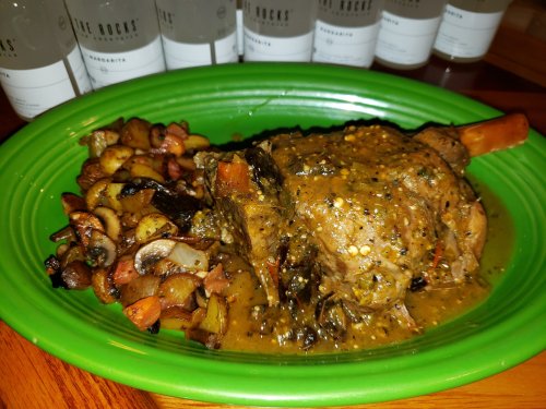 A green plate with a savory lamb shank in sauce, accompanied by a medley of roasted vegetables.