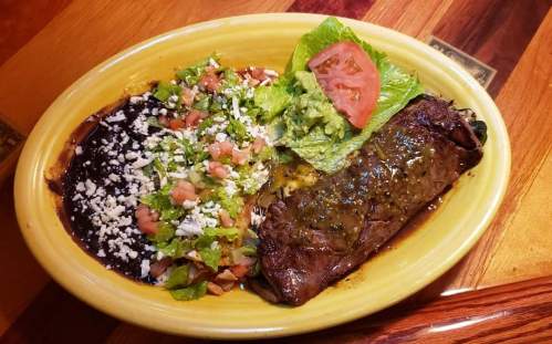 A vibrant plate featuring a beef burrito, black beans, lettuce, tomatoes, guacamole, and cheese on a wooden table.