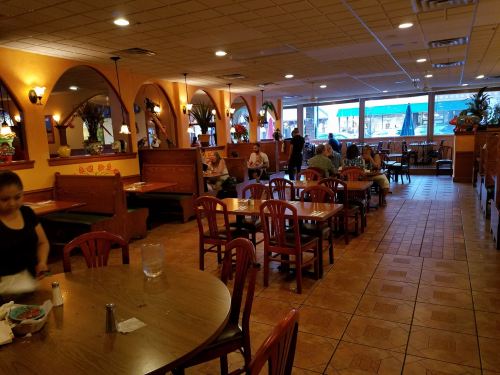 Interior of a restaurant with wooden tables, chairs, and booths; diners enjoying meals and a server attending to tables.