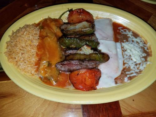 A colorful plate featuring rice, beans, grilled vegetables, and a meat portion with sauce.