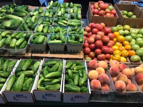 A vibrant display of cucumbers, apples, and peaches in baskets at a market.
