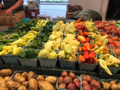 A vibrant display of various peppers and tomatoes in baskets at a market, with potatoes in the foreground.