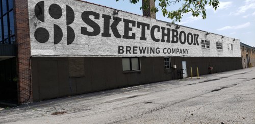 Mural of "Sketchbook Brewing Company" on a brick building, with a clear blue sky above.