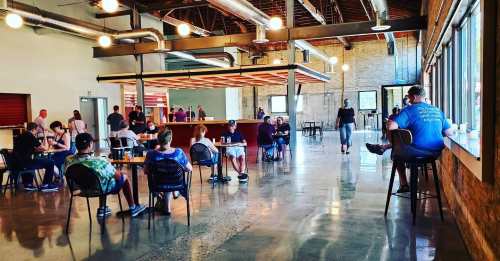 A spacious indoor venue with people seated at tables, enjoying drinks and socializing in a well-lit environment.