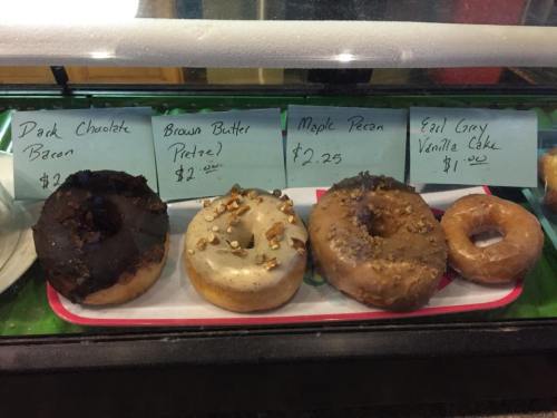 A display of four donuts with labels: Dark Chocolate Bacon, Brown Butter Pretzel, Maple Pecan, and Earl Grey Vanilla Cake.