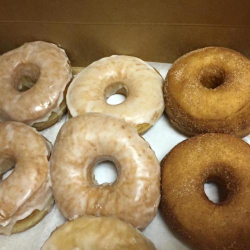 A box of assorted donuts, including glazed and cinnamon sugar varieties, arranged on a white paper lining.