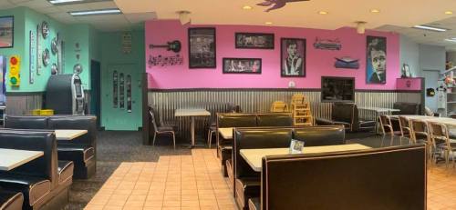 A retro diner interior with black booths, pink walls featuring music-themed art, and a jukebox in the corner.