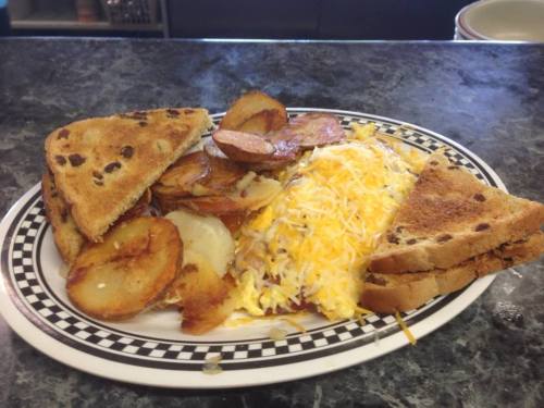 A plate of breakfast featuring scrambled eggs with cheese, fried potatoes, and toasted bread.