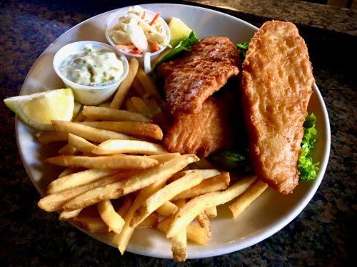 A plate of fried fish fillets with French fries, coleslaw, tartar sauce, and lemon wedges on a bed of lettuce.