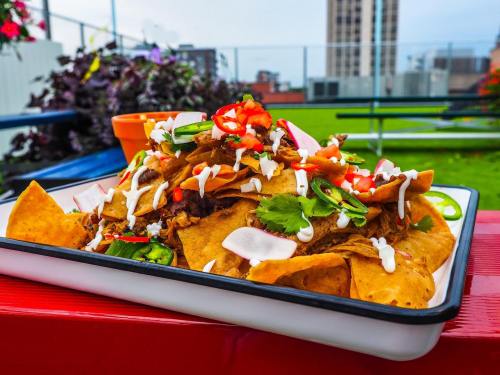 A colorful plate of nachos topped with meat, cheese, jalapeños, cilantro, and drizzled with sour cream.