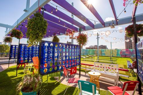 Colorful outdoor seating area with hanging plants, string lights, and vibrant decor under a sunny sky.