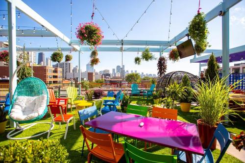 Colorful rooftop garden with vibrant furniture, hanging plants, and a city skyline in the background under a clear blue sky.