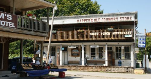 A rustic country store and restaurant with a porch, surrounded by trees and a small outdoor seating area.