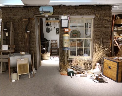 A rustic display featuring a stone wall, vintage tools, and various artifacts in a museum setting.