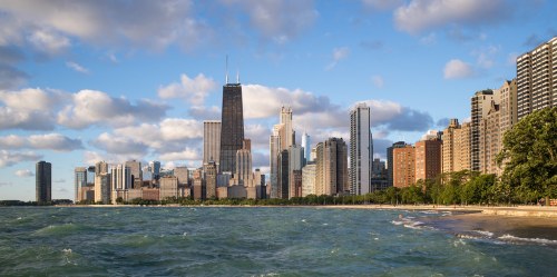 Chicago skyline with tall buildings along the shore of Lake Michigan under a partly cloudy sky.