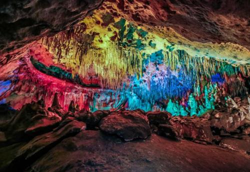 A colorful cave interior with vibrant stalactites and illuminated rock formations in various hues.