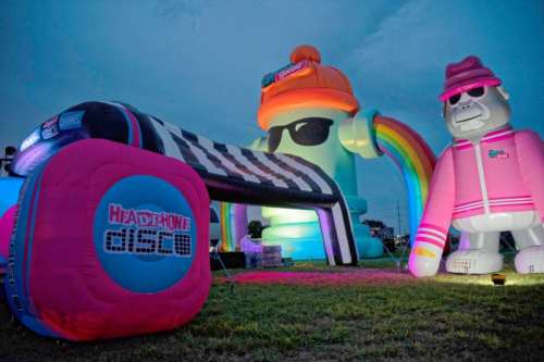 Colorful inflatable structures, including a rainbow and a gorilla, set against a twilight sky at an outdoor event.